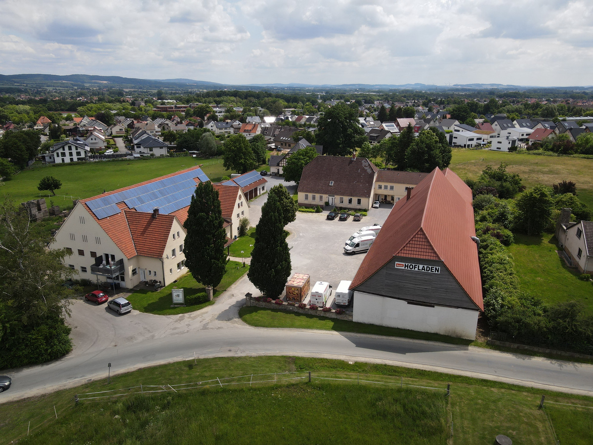 KI generiert: Luftaufnahme eines Hofes mit Gebäuden und Solarpanels, Text: "HOFLADEN".